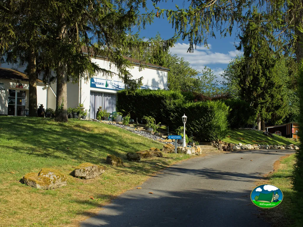 entrada del camping con edificio de recepción, jardín y camino de acceso arbolado