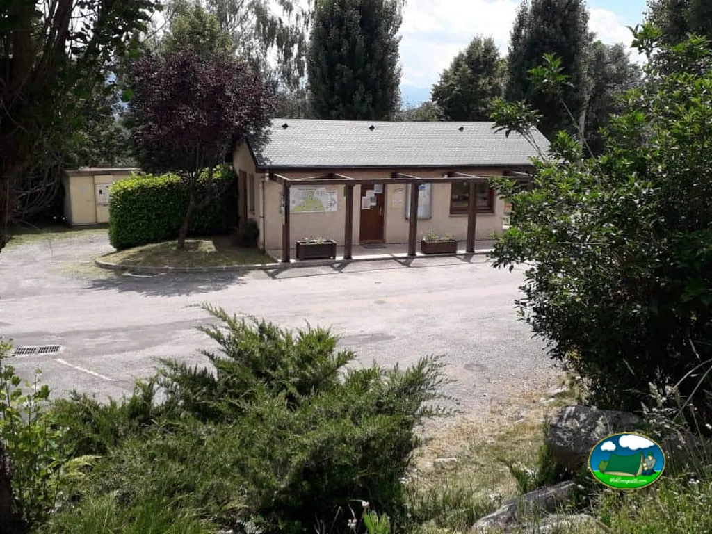 edificio de recepción del camping con tablón de información y aparcamiento arbolado