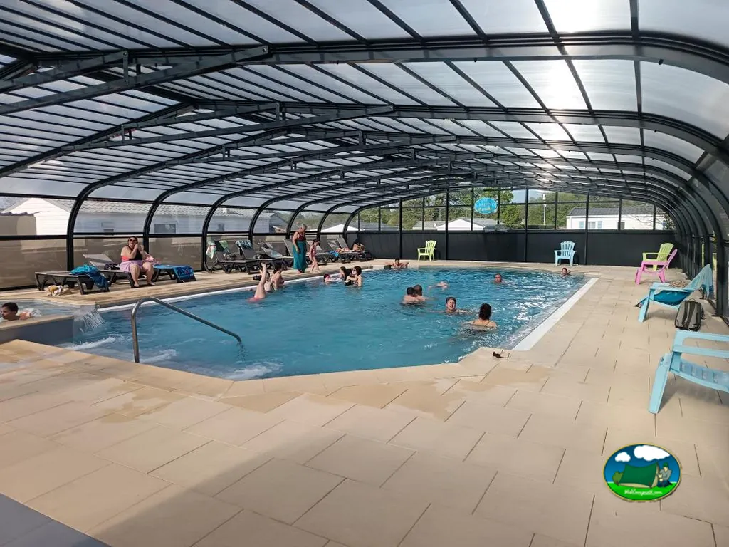 piscina cubierta del camping con bañistas y tumbonas, mobil-homes al fondo