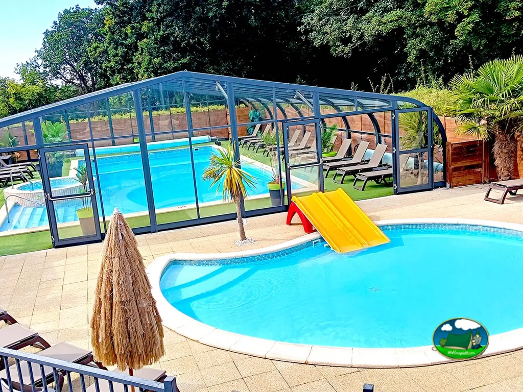 piscina con tobogán infantil junto a la piscina cubierta, rodeadas de palmeras