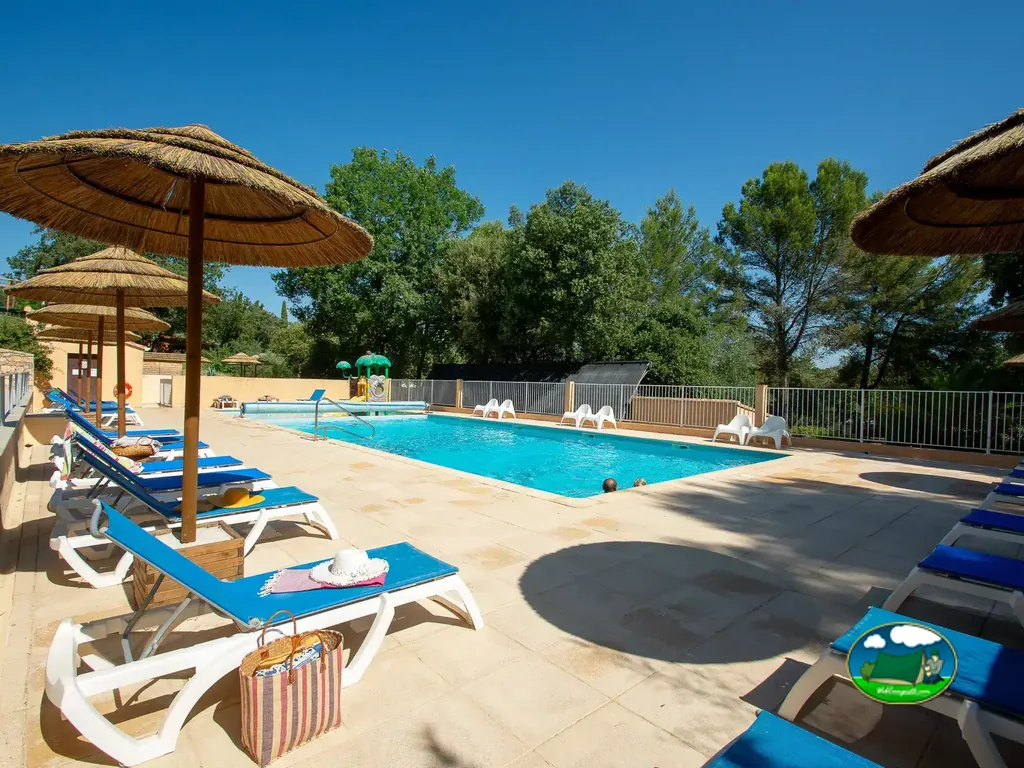 piscina con tumbonas azules y sombrillas de paja junto a un tobogán infantil