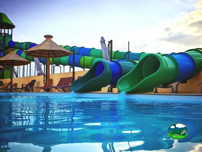 toboganes acuáticos verdes y azules sobre la piscina con sombrillas de paja