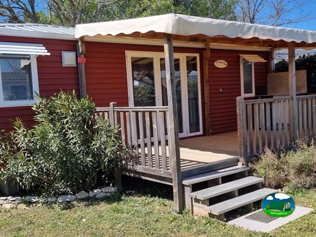mobil-home de fachada roja con terraza de madera cubierta y escalera de acceso