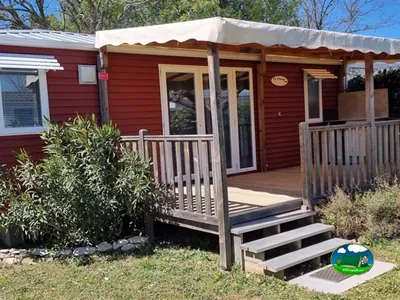 mobil-home de fachada roja con terraza de madera cubierta y escalera de acceso