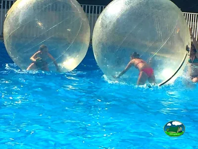 dos personas jugando dentro de burbujas de plástico transparentes en la piscina del camping