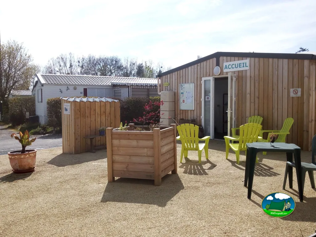 edificio de recepción de madera con terraza y sillas verdes en la entrada del camping