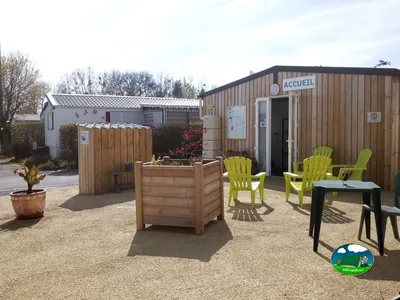 edificio de recepción de madera con terraza y sillas verdes en la entrada del camping