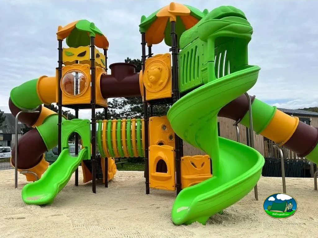 parque infantil con toboganes verdes y naranjas y túneles sobre suelo de arena