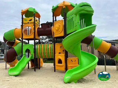parque infantil con toboganes verdes y naranjas y túneles sobre suelo de arena