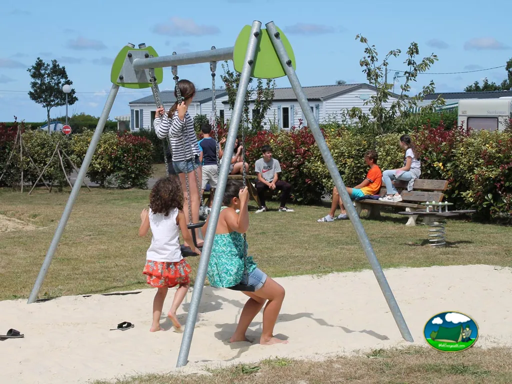niños y niñas jugando en columpios y sentados en un banco junto al parque infantil del camping