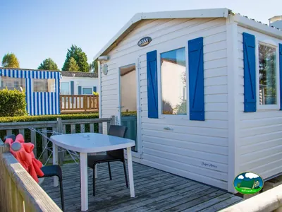 mobil-home de postigos azules con mesa y sillas en la terraza en Auberville