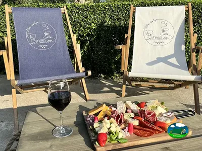 tumbonas de lona con el logo del camping junto a una tabla de quesos y embutidos y una copa de vino en Licques