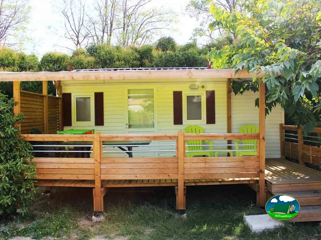 mobil-home con terraza de madera, sillas verdes y contraventanas en Châteaurenard