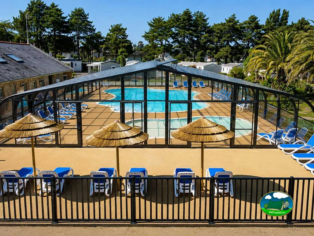 piscina climatizada cubierta con tumbonas azules y sombrillas de paja vacía en Saint-Cast-le-Guildo