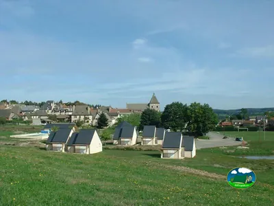 hileras de pequeños chalets de tejado oscuro junto a la piscina, con el pueblo y la iglesia de Marcolès al fondo
