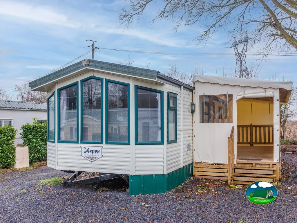 mobil-home con gran ventanal y porche acristalado junto a árboles sin hojas en Gommegnies