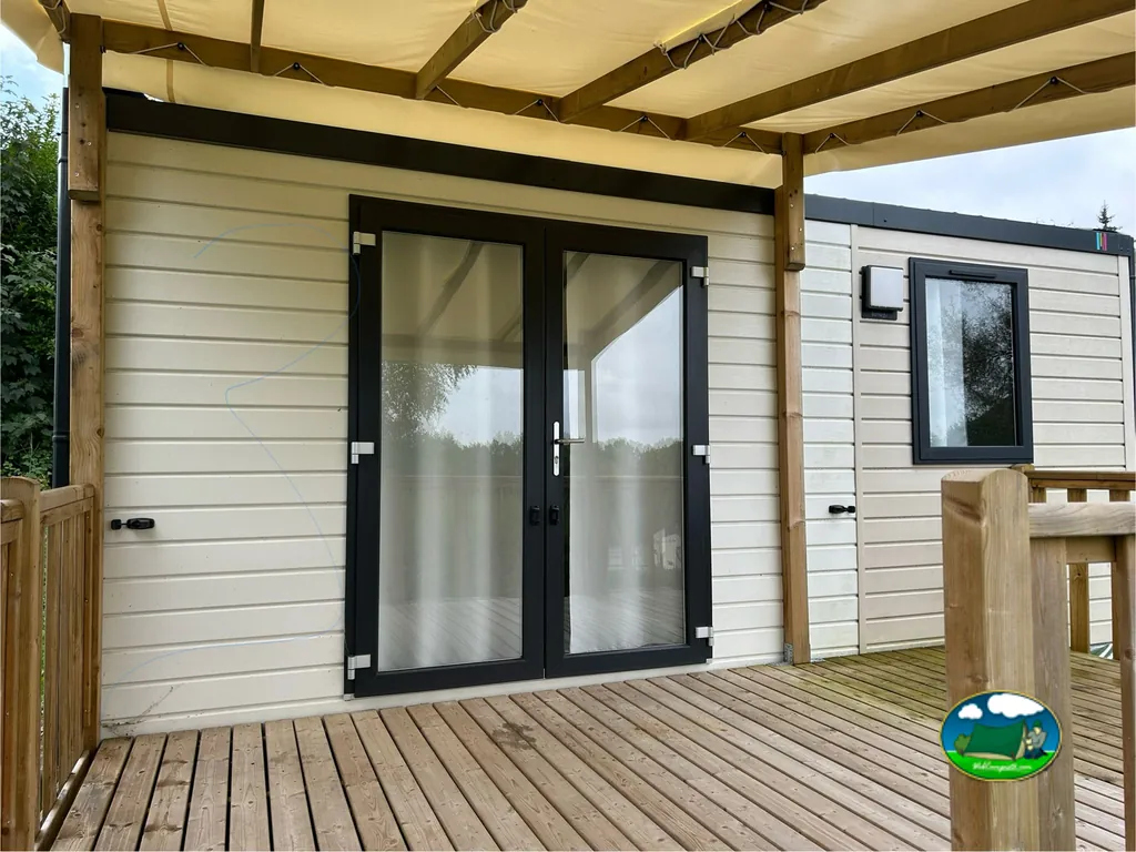 puerta acristalada de un mobil-home bajo un porche de madera con toldo en Grisy-les-Plâtres