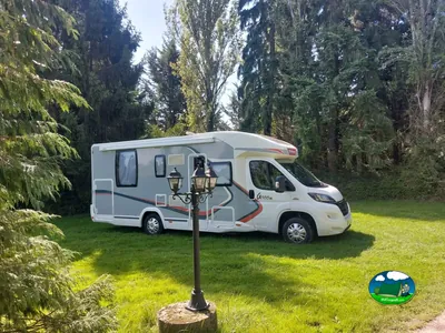 autocaravana aparcada en una parcela de césped entre altos coníferos en Radon