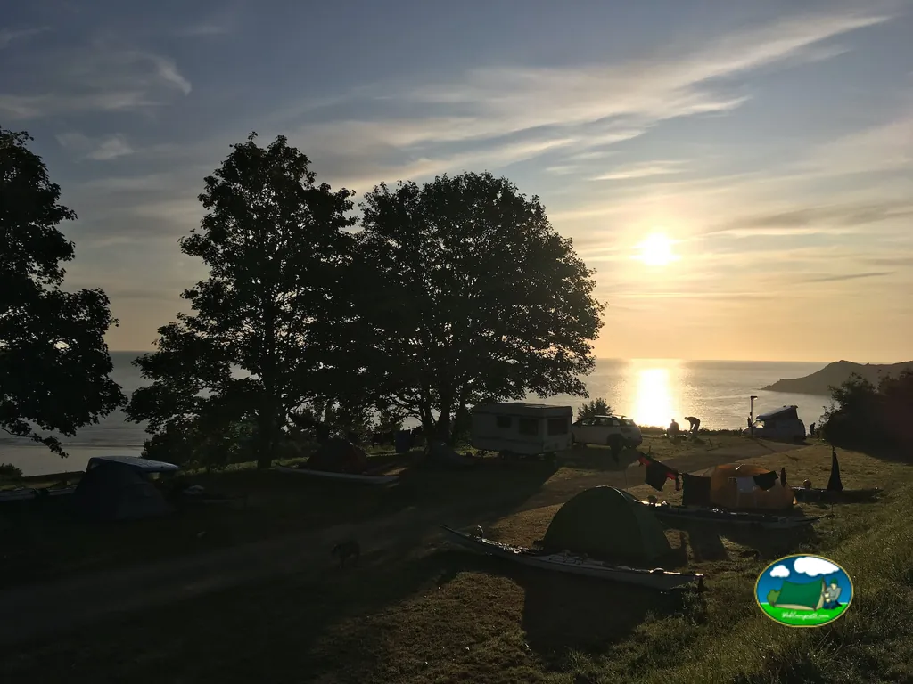 atardecer sobre el mar con tiendas de campaña y una caravana entre árboles en un camping costero de Plouha