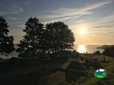 atardecer sobre el mar con tiendas de campaña y una caravana entre árboles en un camping costero de Plouha