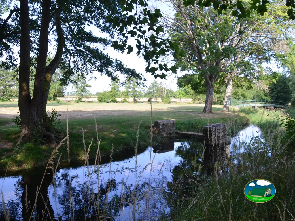 arroyo con un pequeño puente entre árboles en la zona verde del camping de Autun