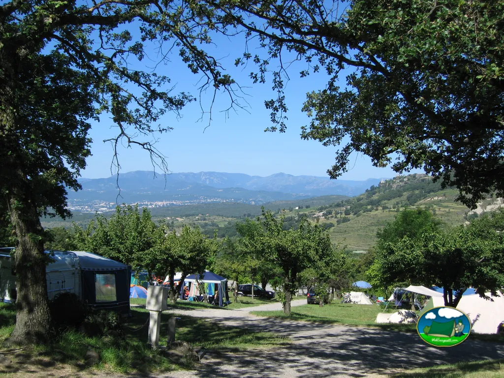 vista elevada de las parcelas del camping con tiendas y caravana entre árboles y colinas en Darbres