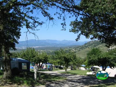 vista elevada de las parcelas del camping con tiendas y caravana entre árboles y colinas en Darbres
