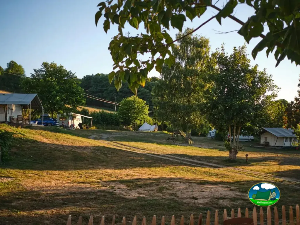 vista general de las parcelas del camping con tiendas y caravanas entre árboles a la luz del atardecer en Crozon-sur-Vauvre