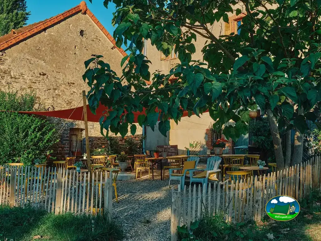 terraza con mesas y sillas bajo un toldo junto al edificio de piedra del camping en Crozon-sur-Vauvre