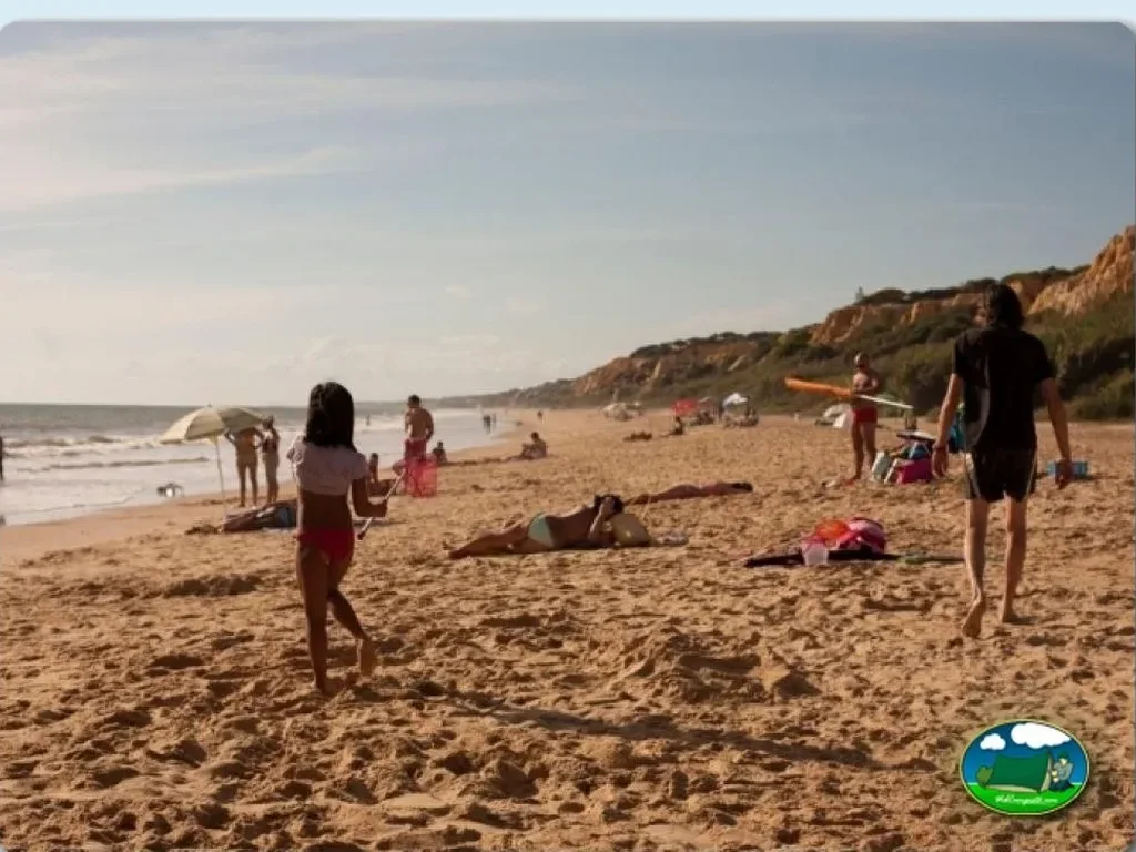 Playa junto al mar con acantilados, familias bañándose y arena del Camping Doñana Playa, Matalascañas (Huelva)