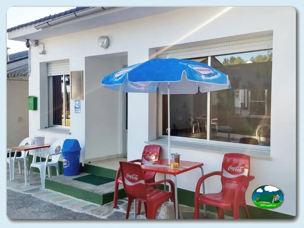 Bar con sombrilla azul y sillas Coca-Cola del Camping El Mesón, Guitiriz (Lugo)
