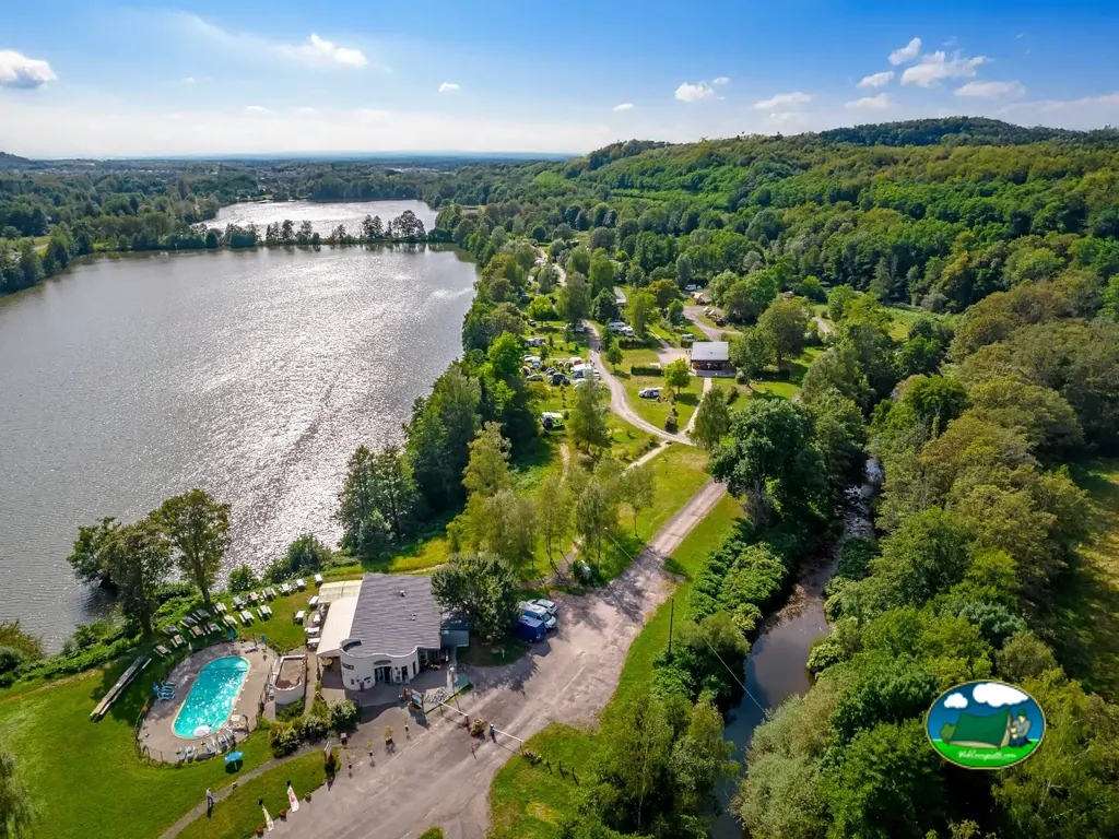 vista aérea del camping junto a un lago con piscina y bungalós entre árboles en Champagney