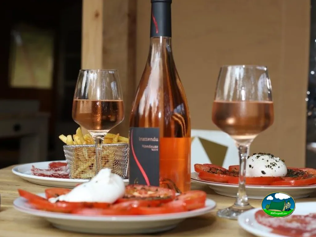 mesa con copas de vino rosado, patatas fritas y tomate con burrata en el restaurante del camping