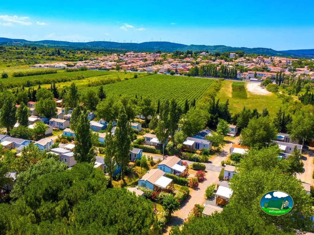 vista aérea del camping entre árboles con viñedos y pueblo al fondo en Sigean