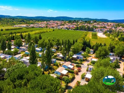 vista aérea del camping entre árboles con viñedos y pueblo al fondo en Sigean