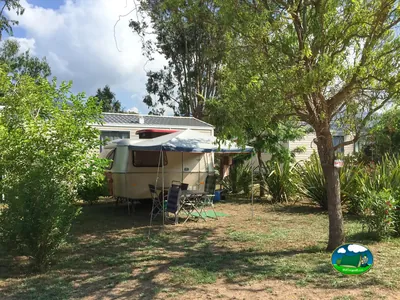 parcela con caravana, toldo y mesa entre árboles en el camping de Viggianello