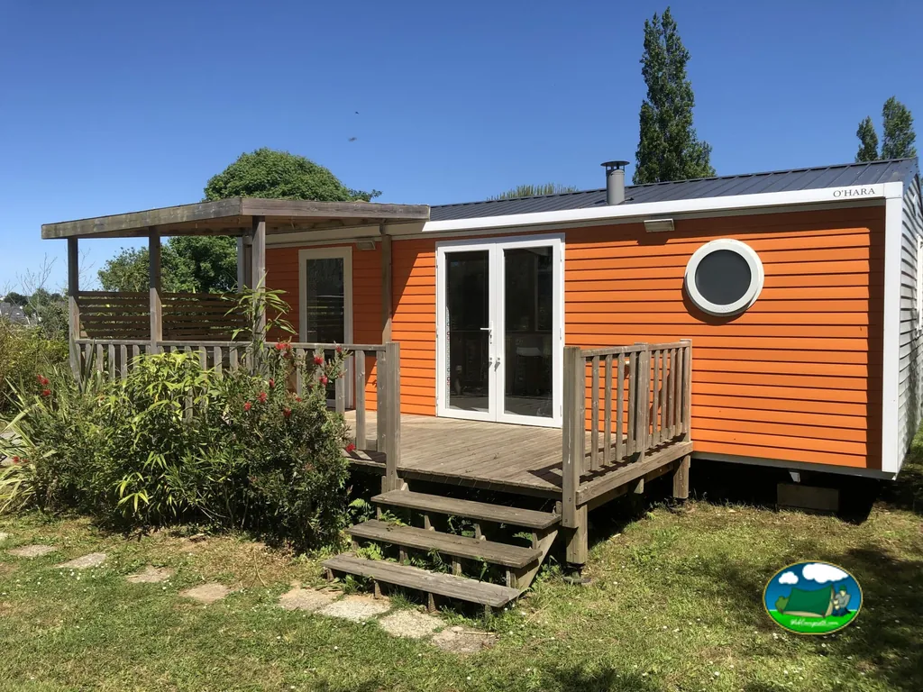 mobile-home naranja con terraza de madera y porche bajo cielo despejado