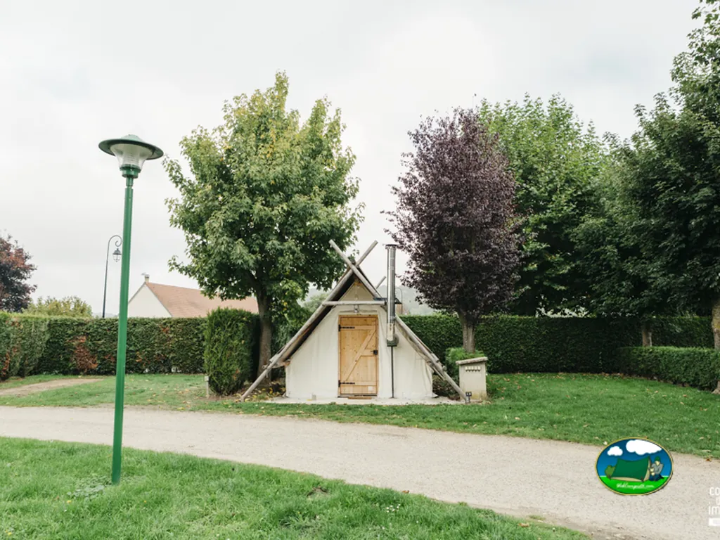 cabaña de lona tipo tipi con chimenea junto a un camino ajardinado
