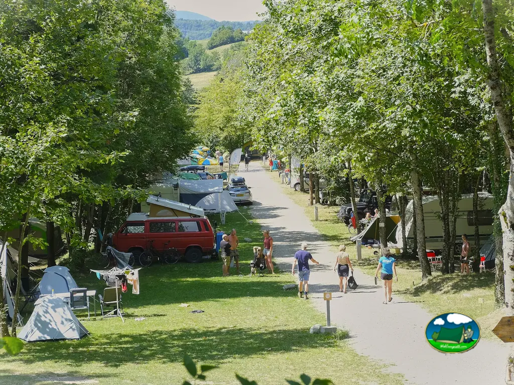 camino arbolado entre parcelas con caravanas, tiendas y campistas paseando