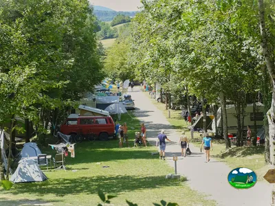 camino arbolado entre parcelas con caravanas, tiendas y campistas paseando