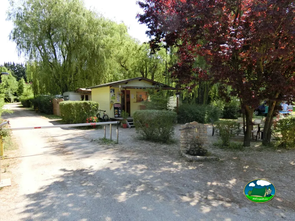 entrada del camping con barrera, recepción y zona de mesas bajo los árboles