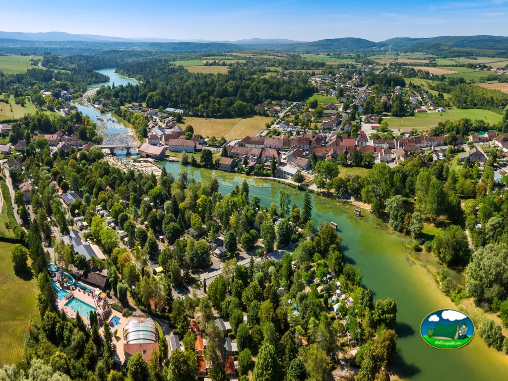 vista aérea del camping junto al río con piscina, tobogán y el pueblo alrededor