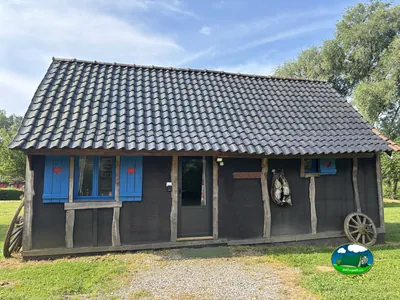caseta de madera oscura con contraventanas azules decoradas con corazones y una rueda de carro antigua
