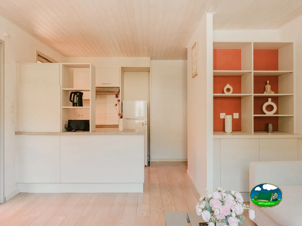 interior de un alojamiento con cocina abierta y estantería decorativa en tonos crema y naranja