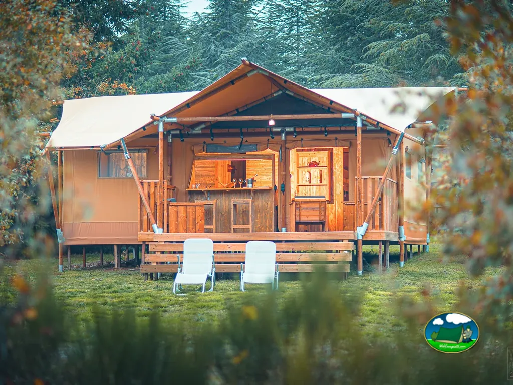 tienda de glamping con porche de madera, barra y tumbonas enmarcada por follaje otoñal