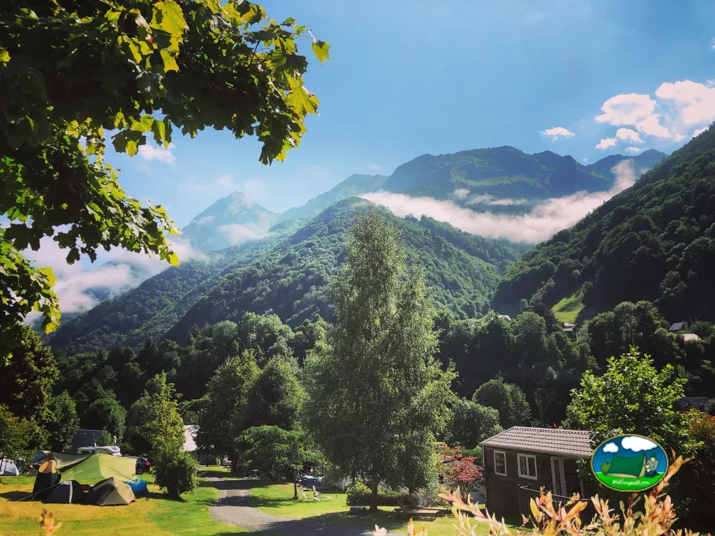 parcelas de acampada con tienda de campaña y cabaña de madera frente a montañas con niebla en Cauterets