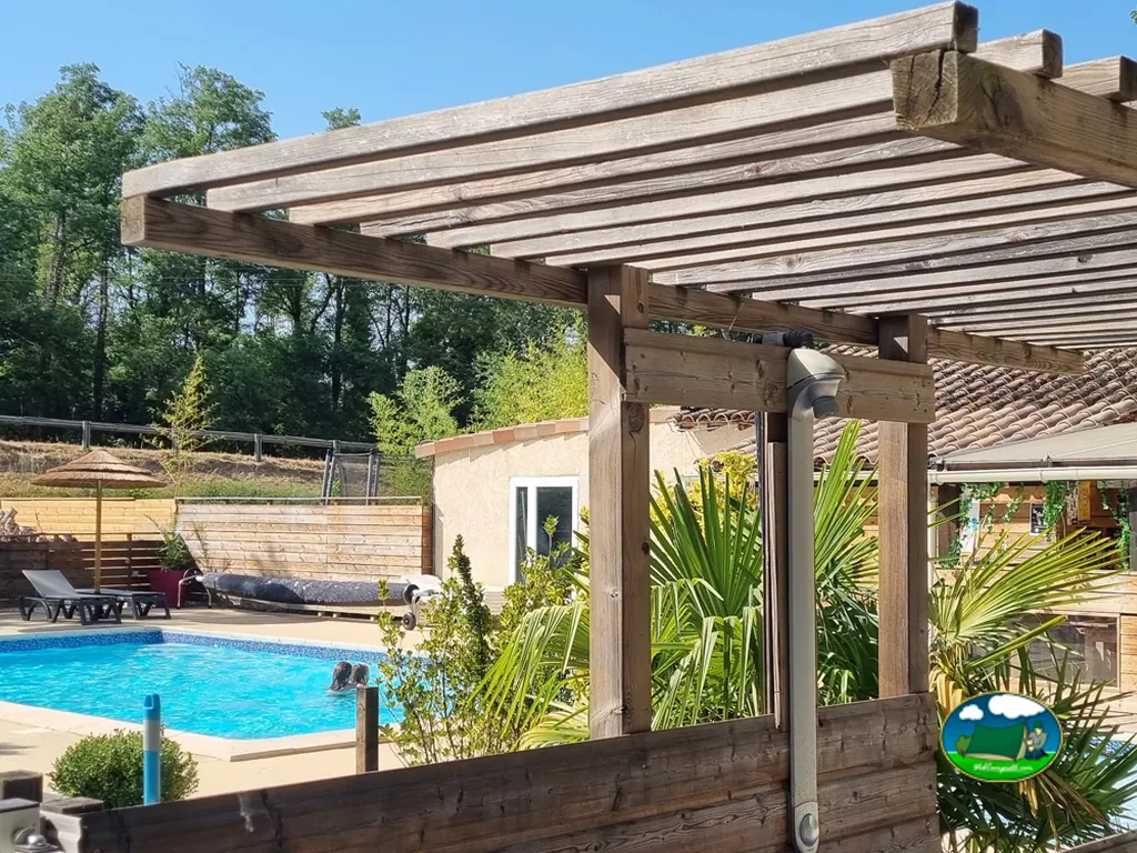 piscina vista bajo una pérgola de madera con personas bañándose en Ruoms