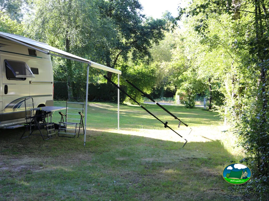 parcela con avancé de autocaravana y sillas de camping bajo grandes árboles en Fougères