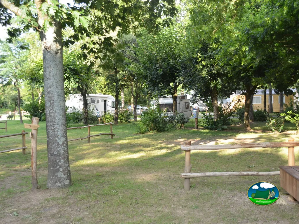 parcelas sombreadas por árboles con caravanas y autocaravanas estacionadas tras una valla de madera