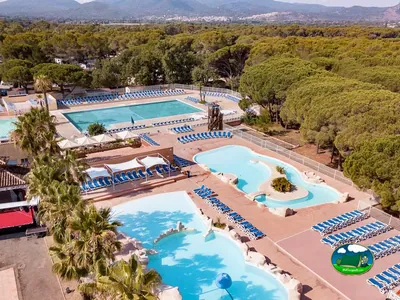 vista aérea del complejo de piscinas con tumbonas, jardín de pinos y montañas al fondo
